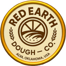 A circular logo with a golden border, featuring the text "Red Earth Dough Co." and "Alva, Oklahoma, USA." In the center, there is an illustration of a rising sun over fields, flanked by two wheat stalks.